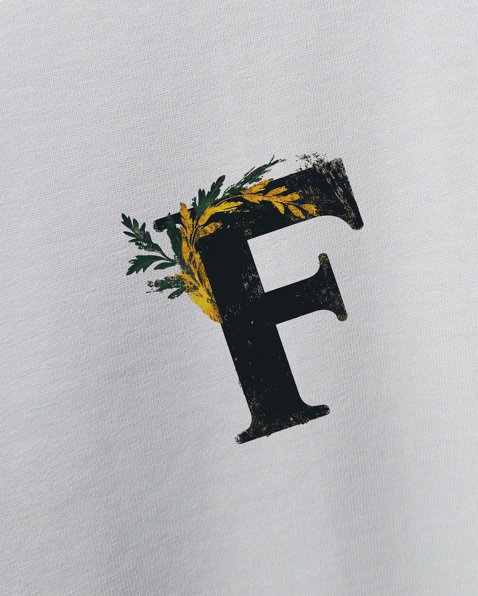 Ancient Ambition Vintage Beyaz Oversize Tişört, Beyaz bir tişört üzerinde, yeşil ve sarı yapraklarla süslenmiş, eskitilmiş görünümlü, büyük siyah bir 'F' harfi. -  Faylit