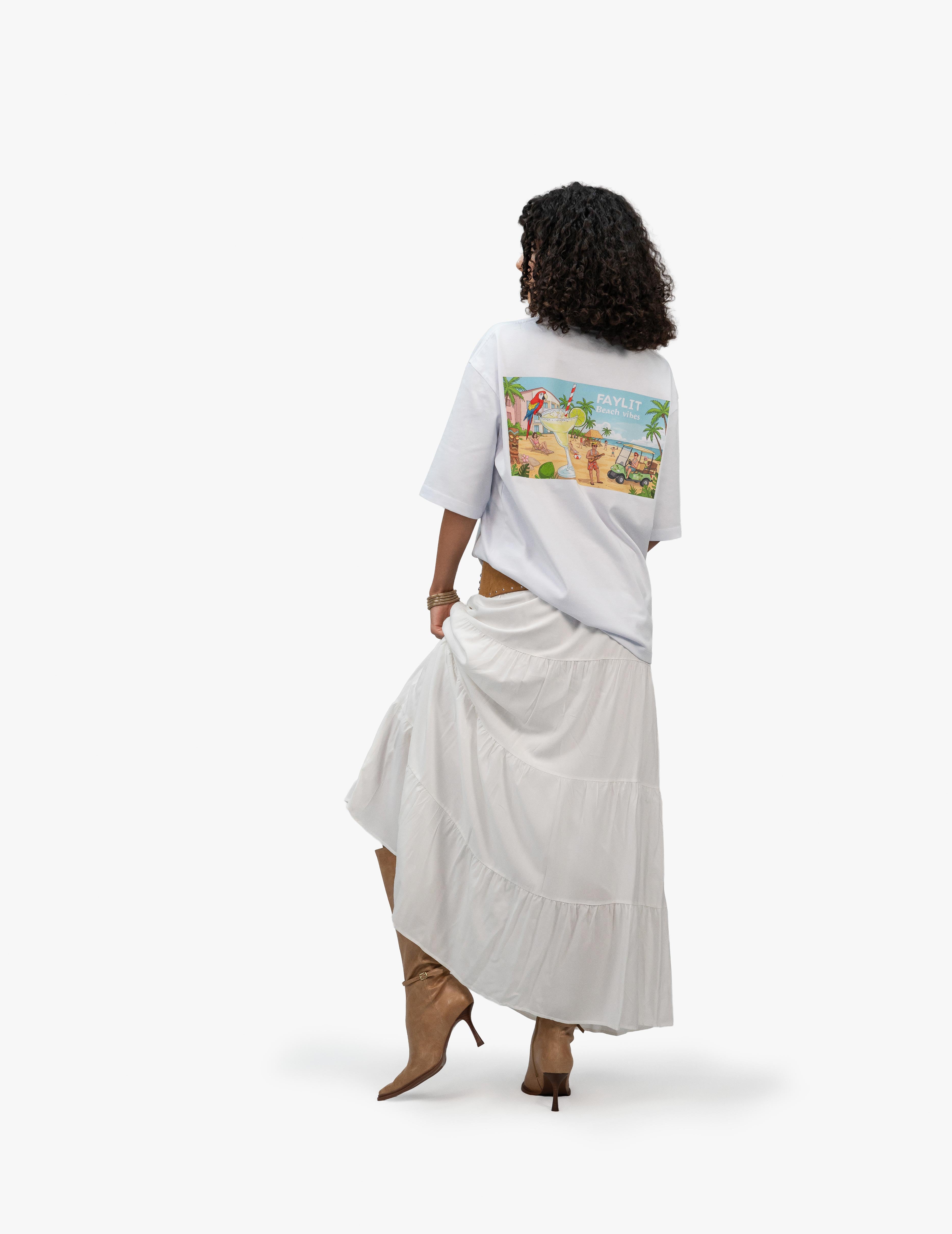 Beach Vibes Optik Beyaz Oversize Unisex Tişört, Beyaz bir fonun önünde, arkası dönük ve hafifçe sola dönük duran, kısa siyah kıvırcık saçlı bir kadın. Üzerinde sırt kısmında palmiyeler, bir papağan ve bir golf arabası içeren plaj temalı renkli bir grafik baskı bulunan beyaz, geniş kesim bir tişört ve uzun, beyaz, kat kat bir etek giyiyor. Ayaklarında sivri burunlu, açık kahverengi, topuklu botlar bulunuyor. -  Faylit