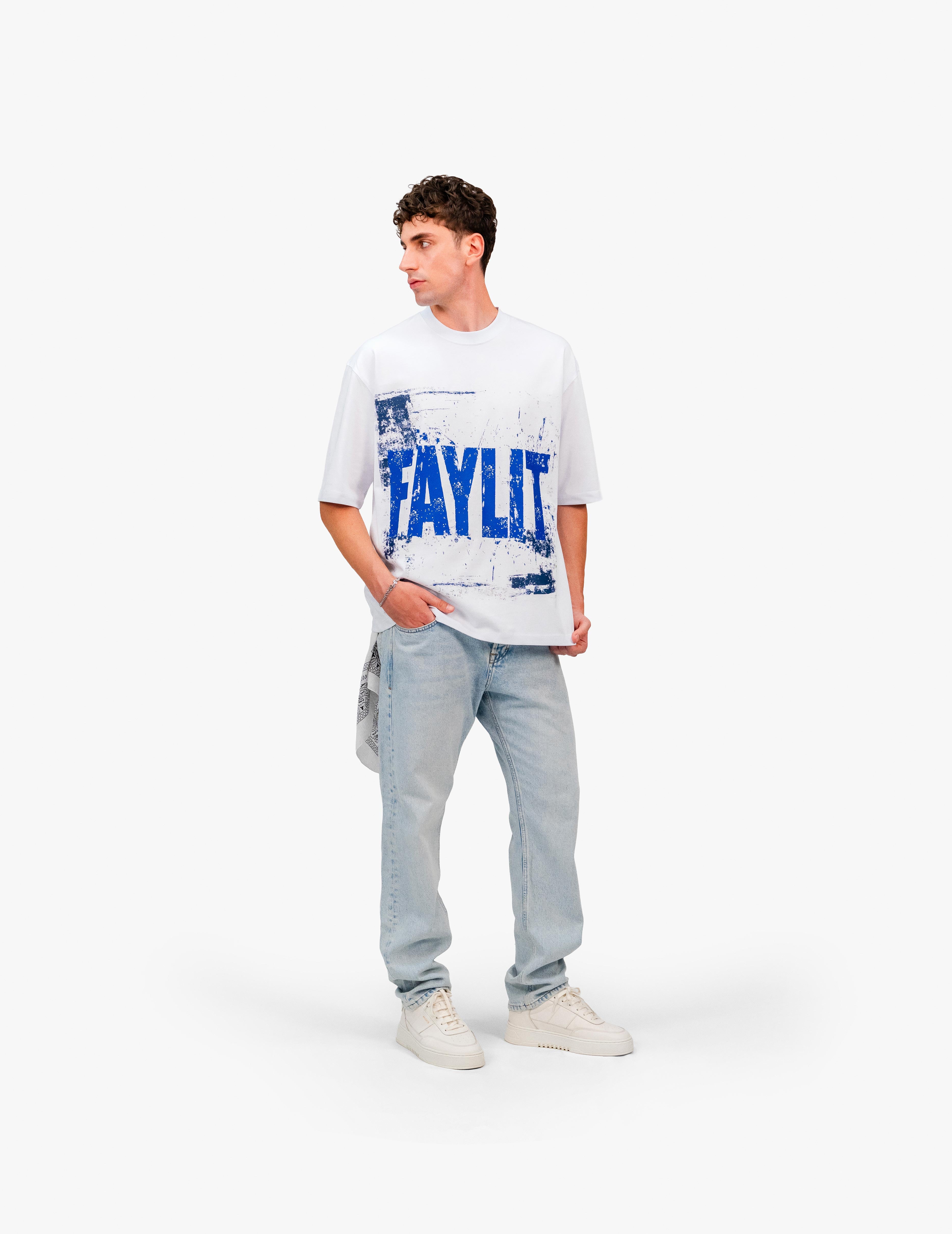00Blue Optik Beyaz Oversize Tişört Beyaz stüdyo fonunda, yana dönük poz veren erkek manken. Üzerinde, mavi "FAYLIT" baskılı beyaz oversize tişört ve açık renkli, bol kesim kot pantolon giyiyor. Kombin, beyaz spor ayakkabılarla tamamlanmış. Arka cebinden desenli bir mendil/bandana sarkıyor. -  Faylit