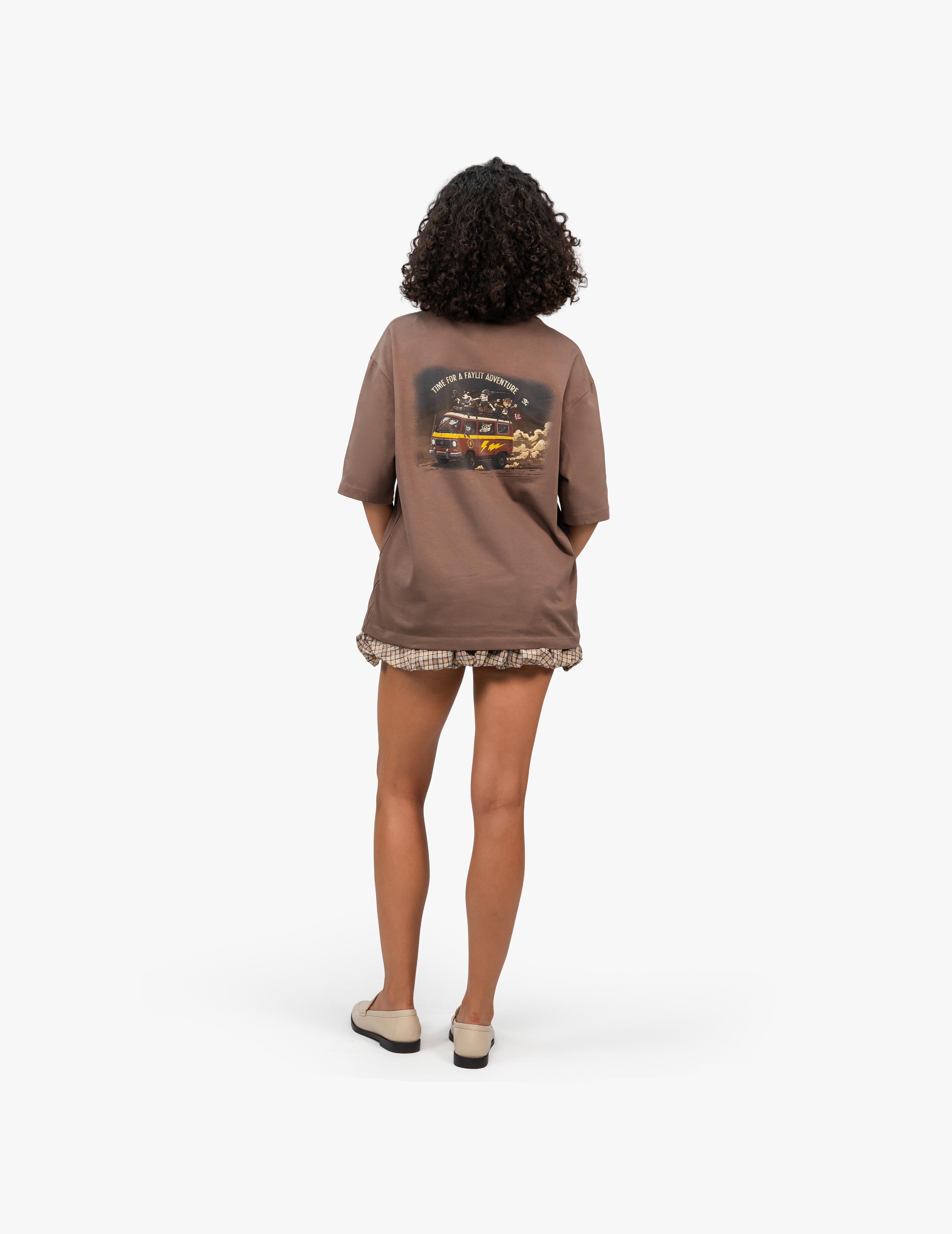 Adventure Kahverengi Oversize Unisex Tişört, Beyaz bir stüdyo fonunun önünde, arkası dönük bir şekilde duran, kısa siyah kıvırcık saçlı bir kadın. Üzerinde sırtında renkli bir grafik baskı bulunan kahverengi, geniş kesim bir tişört ve etek ucu fırfırlı, kahverengi ekose desenli bir şort giyiyor. Ayaklarında açık renk loafer ayakkabılar var. -  Faylit