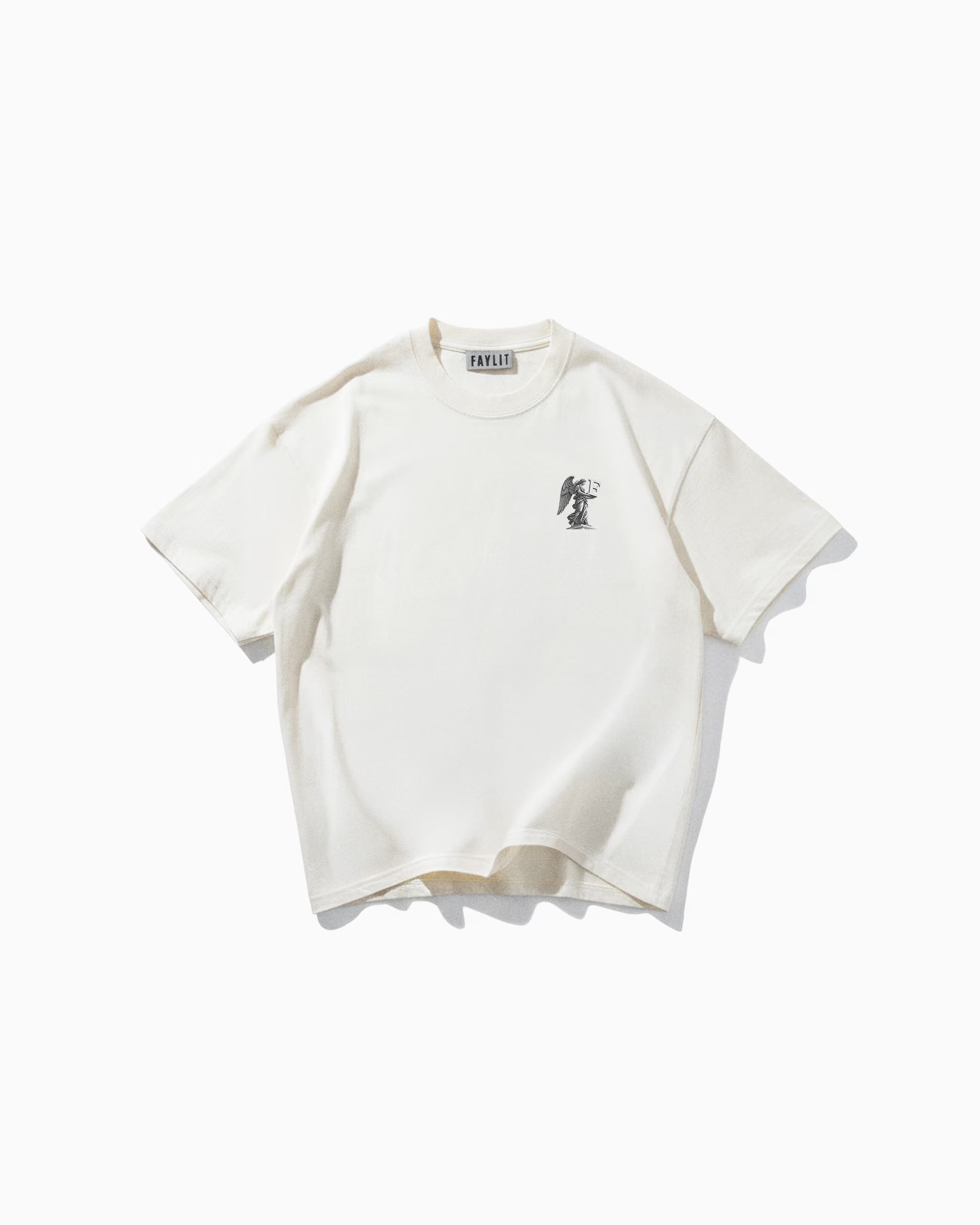 Angel Off White Oversize Tişört - Krem rengi (Off White) oversize tişörtün düz çekim ürün fotoğrafı. Tişörtün sol göğüs kısmında, siyah-beyaz detaylı bir baskı yer alıyor. Baskıda, elinde kılıç ve terazi tutan, zırhlı ve kanatlı bir melek (Başmelek Mikail) figürü resmedilmiş. Yaka içindeki "Faylit" marka etiketi görülebilmektedir.