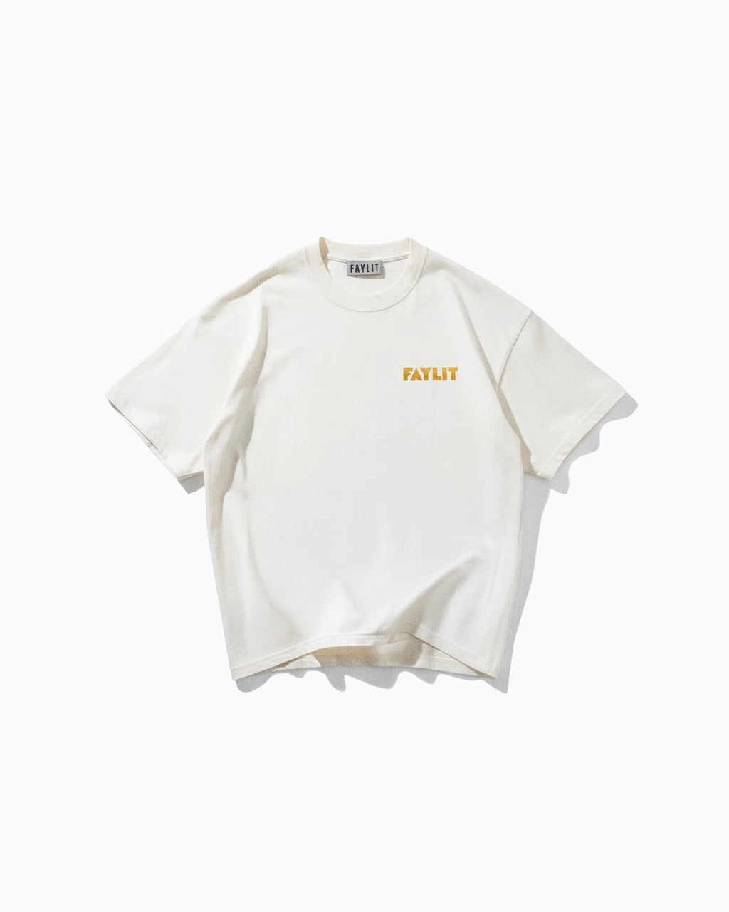Bee Off White Oversize Tişört Kırık beyaz (off-white) oversize tişörtün ön yüzünün düz çekim ürün fotoğrafı. Tişörtün sol göğüs kısmında, hardal sarısı renginde, minimalist ve modern bir fontla "FAYLIT" yazmaktadır. Yaka içindeki marka etiketi de görülebilmektedir.