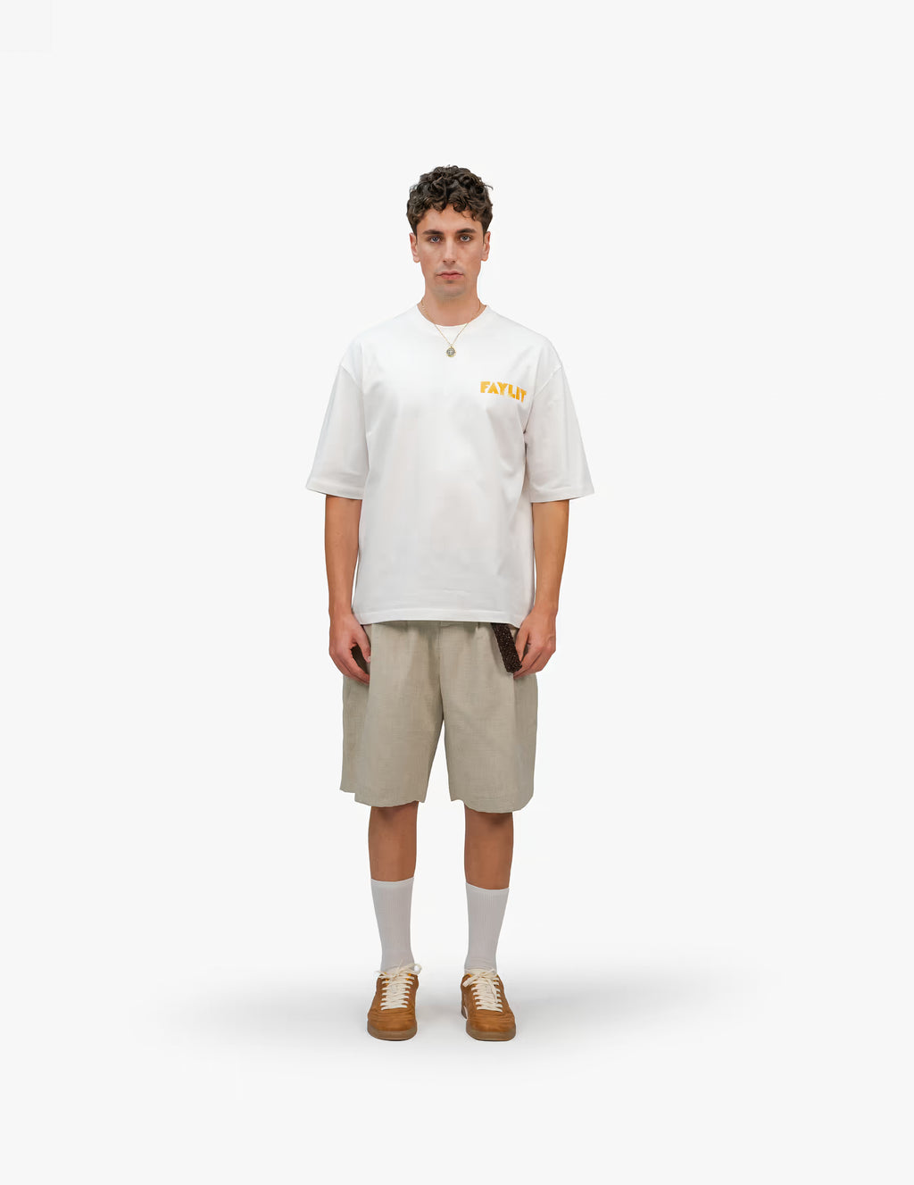 Erkek modelin üzerindeki FAYLIT oversize beyaz t-shirt, göğüste turuncu FAYLIT logosu, şort ve spor ayakkabı ile kombinlenmiş, rahat ve şık günlük giyim.