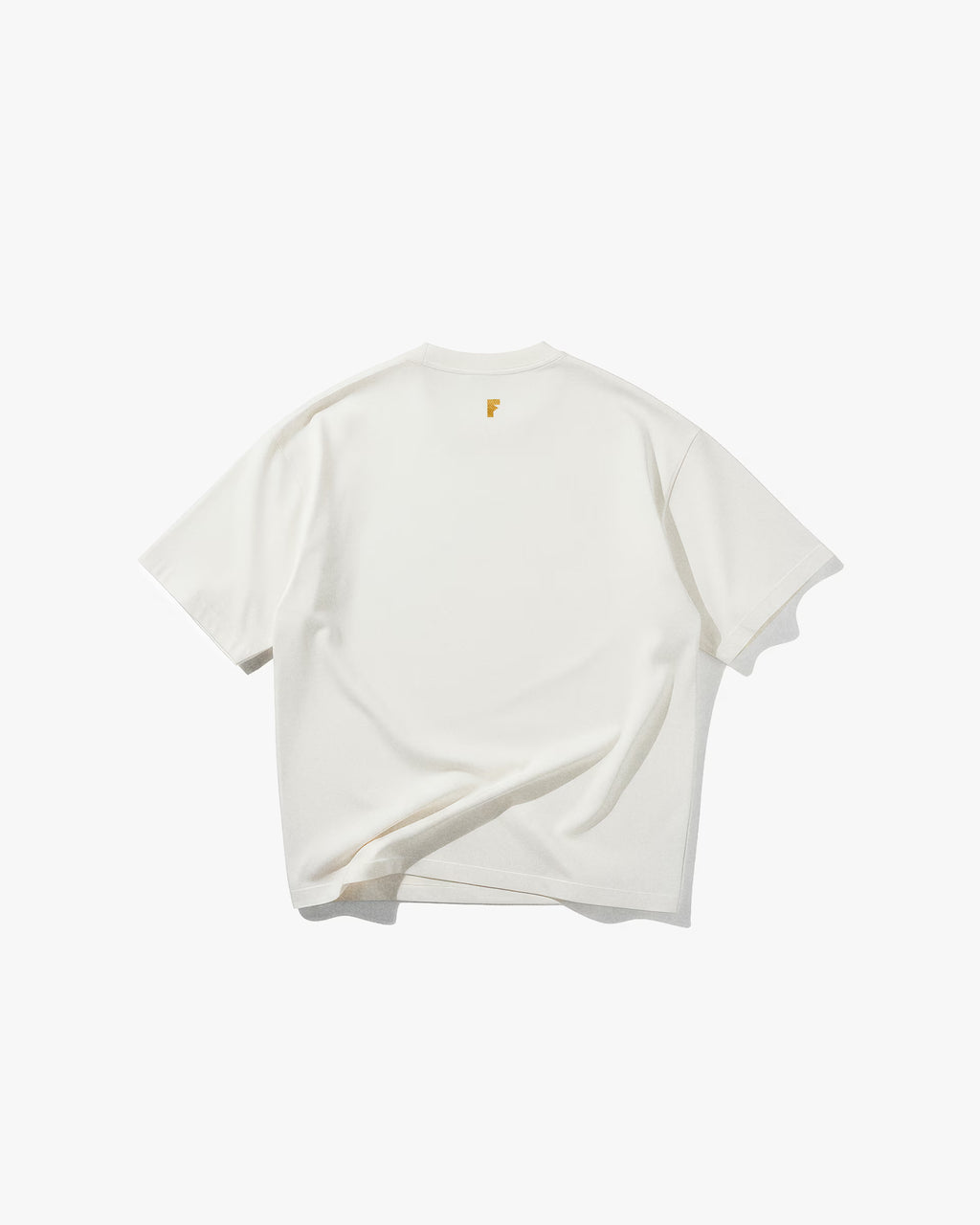 Bee Off White Oversize Tişört Kırık beyaz (off-white) oversize tişörtün sırt yüzeyinin düz çekim ürün fotoğrafı. Tişörtün ensesinin altında, hardal sarısı renginde, küçük ve modern bir 'F' harfi logosu bulunmaktadır. Tasarım, minimalist ve sadedir.