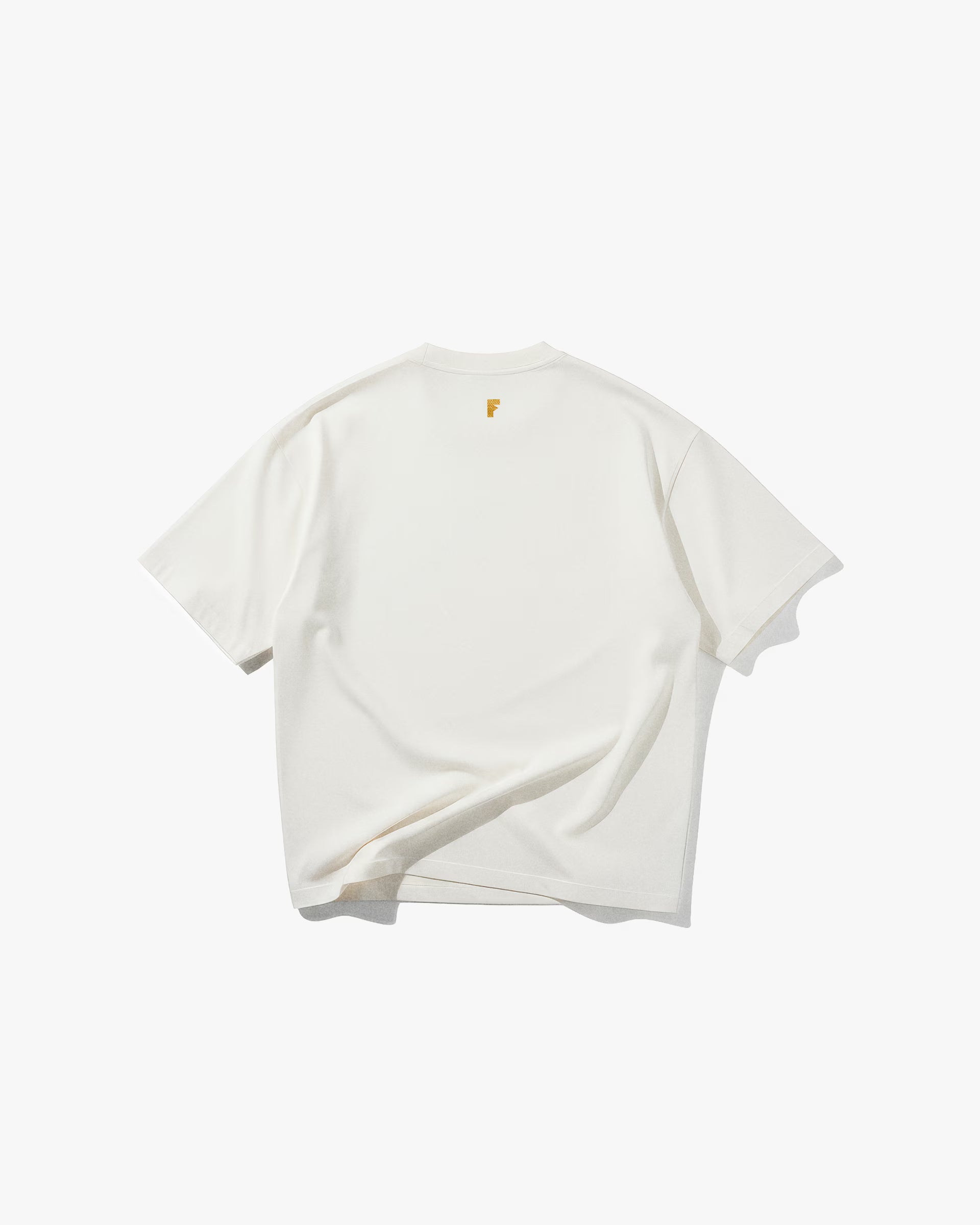 Bee Off White Oversize Tişört Kırık beyaz (off-white) oversize tişörtün sırt yüzeyinin düz çekim ürün fotoğrafı. Tişörtün ensesinin altında, hardal sarısı renginde, küçük ve modern bir 'F' harfi logosu bulunmaktadır. Tasarım, minimalist ve sadedir.