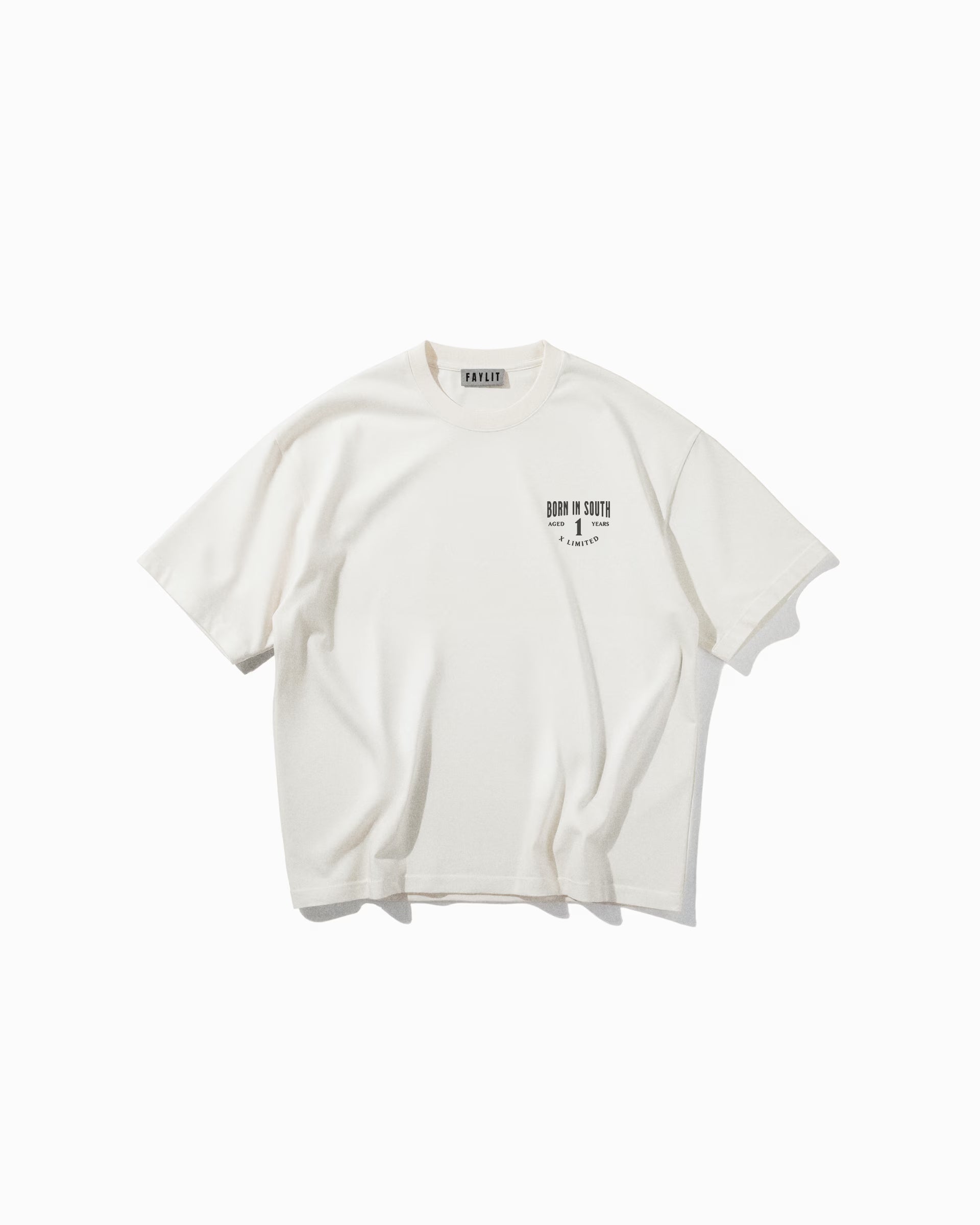 Culture Off White Oversize Tişört Kırık beyaz (off-white) oversize tişörtün ön yüzünün düz çekim ürün fotoğrafı. Tişörtün sol göğüs kısmında, siyah renkte küçük bir logo baskısı yer alıyor. Baskıda, eskitme efektli ve kalın bir fontla "FAYLIT" yazmaktadır. Yaka içindeki marka etiketi de görülebilmektedir.