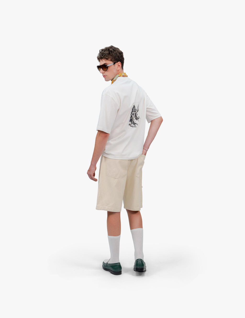 Gods Off White Oversize Tişört Beyaz stüdyo fonunda, arkası dönük duran ve omzunun üzerinden geriye bakan erkek manken. Sırtında, dikey ve gravür stilinde meleklerin mücadelesini tasvir eden bir baskı bulunan beyaz oversize tişört giyiyor. Kombini, bej rengi şort, beyaz çorap ve siyah makosen ayakkabılarla tamamlanmış. Boynundaki yeşil fular ve taktığı güneş gözlüğü de görülüyor. -  Faylit