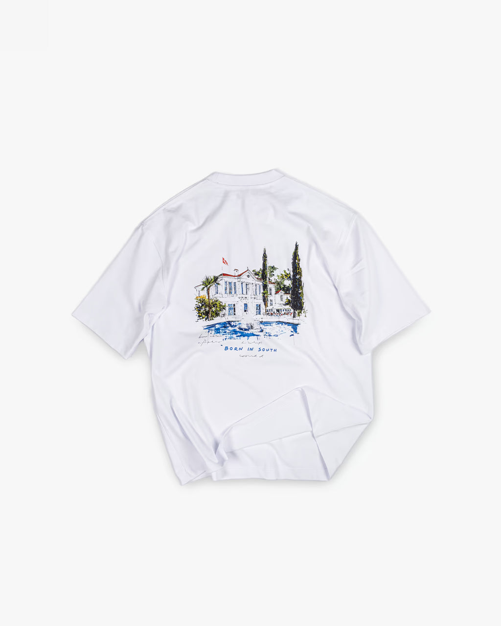 FAYLIT beyaz oversize tişört, arka kısmında Born in South temalı, Akdeniz stili beyaz ev ve ağaç figürleri içeren renkli grafik baskı, unisex ve rahat kesim, günlük giyim için ideal.