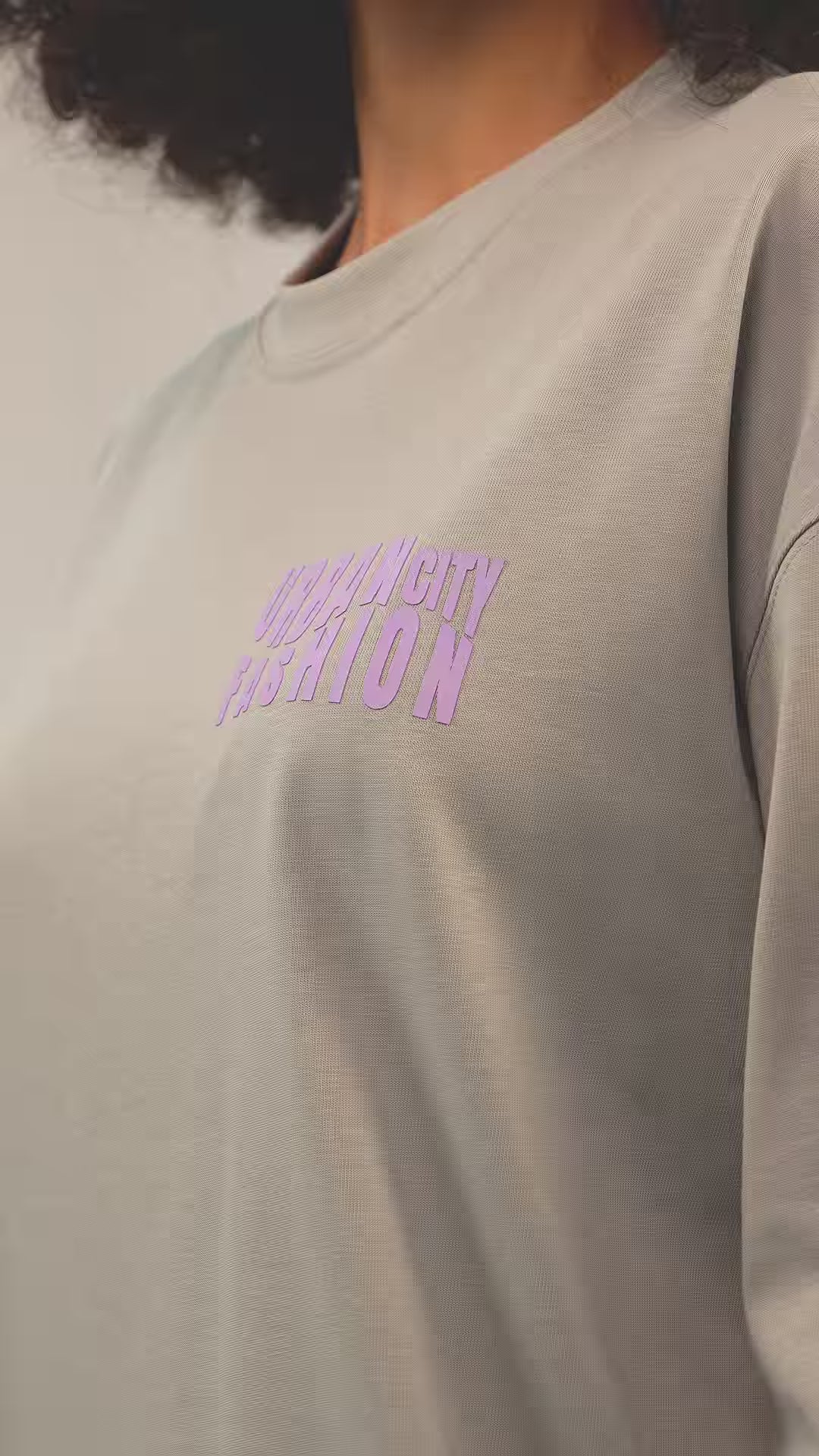 Faylit Urban Essential Limited Edition Gri oversize Premium tişört giyen kıvırcık saçlı fotomodel, tişörtün arkasında Faylitin mottosu ve kuruluş tarihi yazıyor. Ön kısmında ise Urban City Fashion yazısı kabartma bir şekilde görünüyor. Mankenin Son model güneş gözlüğü oldukça iddaalı