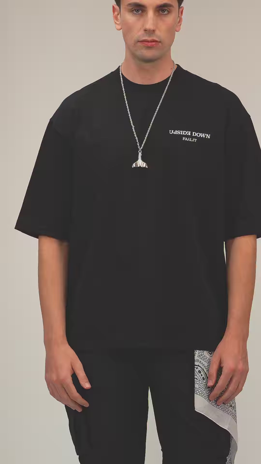 Faylit Siyah Upside Down oversize premium tişört giyen foto model balina kuyruğu tasarım bir kolye takıyor. Beyaz bir mendille tamamlanmış bu kombinin alt üst edilmiş tişört tasarımı ve baskısı oldukça dikkat çekici